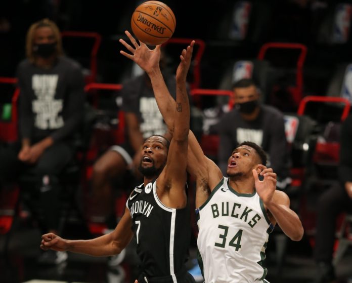 Nets and Bucks stars Durant and Giannis rising up for the jump ball.